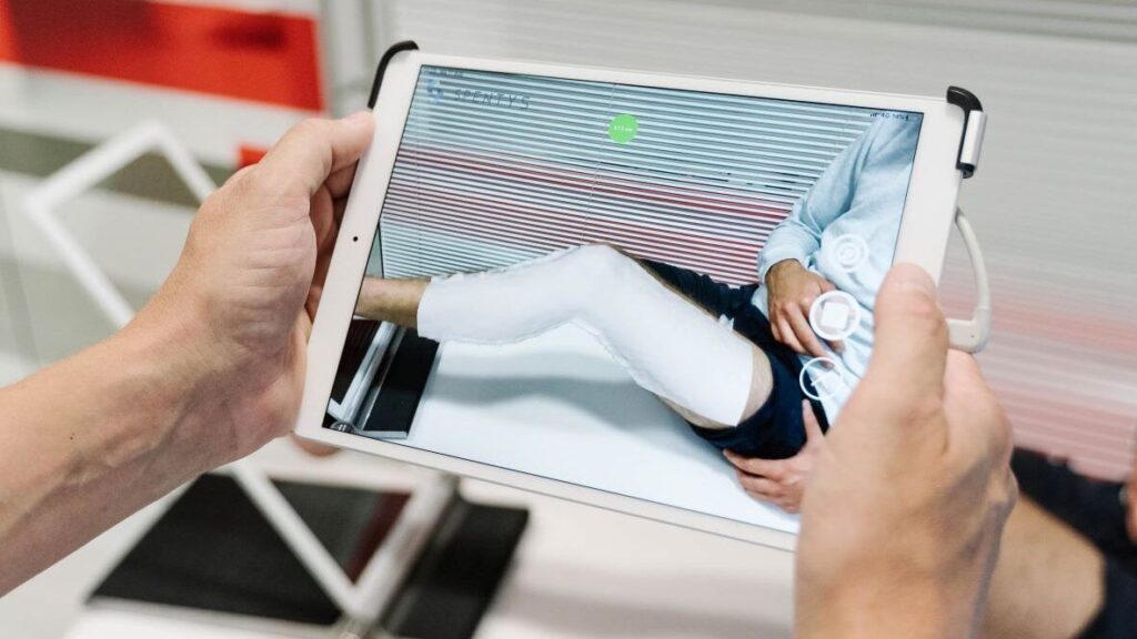 Person holding tablet device to view leg injury in medical office.